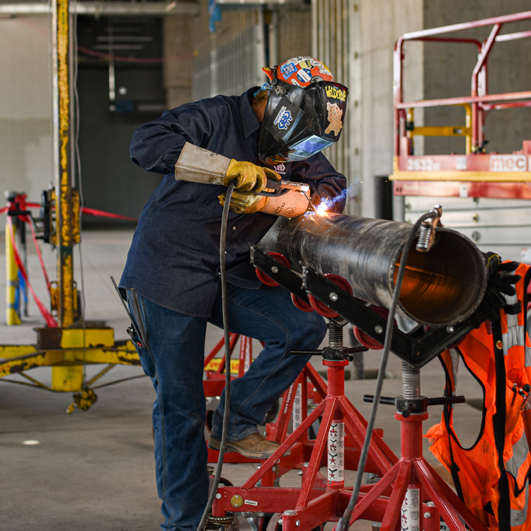 A woman welder welding on a big pipe wearing Justin women’s work boots.